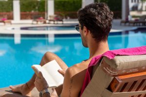 A Guy enjoying his Book in the sun by the Pool.